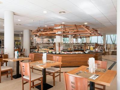 Spacious hotel dining area with wooden tables and buffet counter under a large wooden canopy.