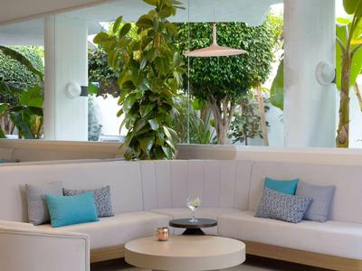 Moderne Sitzecke mit weißen Sofas, blauen Kissen und grünen Pflanzen im Hintergrund.