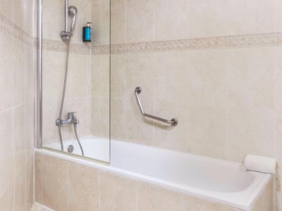 Ein helles Badezimmer mit Badewanne, Duscharmatur und Handtuchhalter an der Wand.