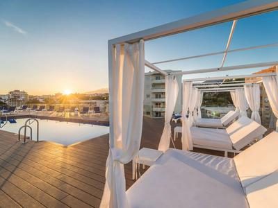 Luxuriöse Liegen mit Vorhängen neben einem Pool bei Sonnenuntergang in einem Hotelresort.