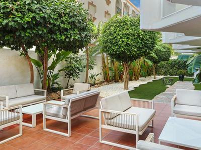 Außenbereich eines Hotels mit weißen Sitzmöbeln, roten Fliesen und gepflegtem Garten.