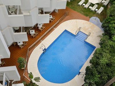 Hotelpool in ockerfarbenem Hof mit weißen Liegestühlen und grünen Pflanzen umgeben.