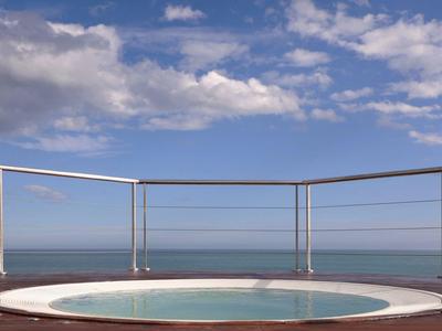 Runder Whirlpool auf einer Terrasse mit Meerblick und blauem Himmel.