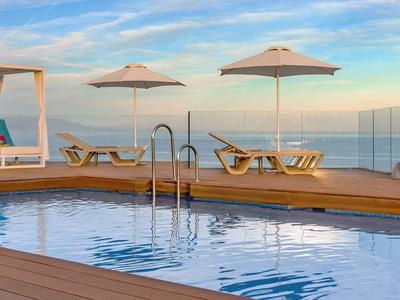 Moderner Hotelpool mit Sonnenliegen und Schirmen mit Meerblick am Abend.