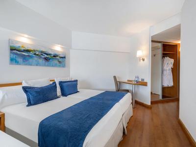 Helles Hotelzimmer mit Doppelbett, blauem Bettläufer, Kissen und Holzboden.