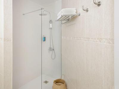 Helles, schlichtes Badezimmer mit begehbarer Dusche, Handtüchern und Haken an der Wand.