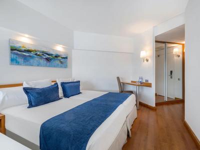 Modernes Hotelzimmer mit Doppelbett, blauen Akzenten und Schreibtisch neben dem Eingang.