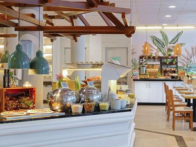 Modernes Hotelrestaurant mit Kaffeeautomat, Kuchen und Sitzbereichen in hellem Ambiente.
