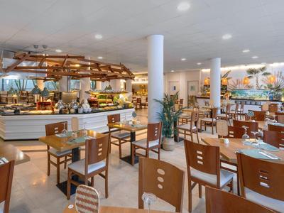Helles Hotelrestaurant mit Holzstühlen, Tischen und Buffetbereich im Hintergrund.
