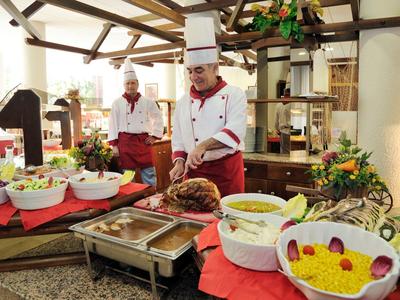 Chefs serve food at a buffet with various dishes and vibrant decor indoors.