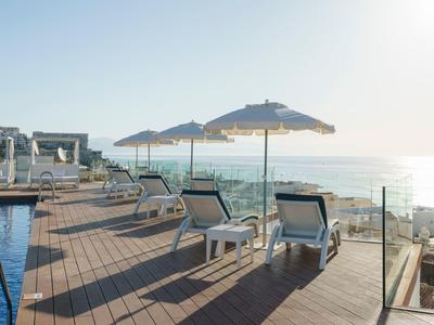 Sun loungers and umbrellas on a wooden deck by a pool overlooking the sea at sunrise.