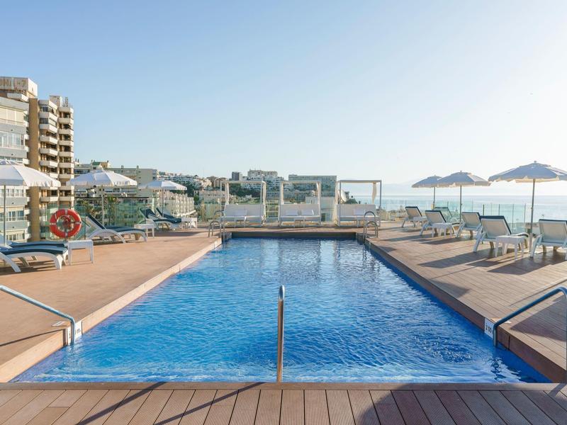 Outdoor hotel pool with sun loungers and umbrellas under clear blue sky.