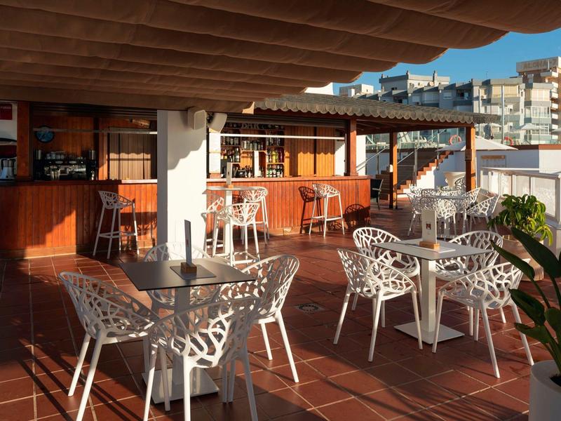 Outdoor terrace with white metal tables and chairs, overhead wooden beams, city view