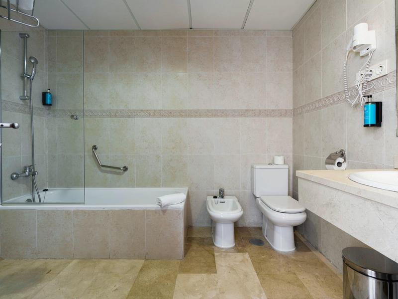 Modern bathroom with bathtub, toilet, bidet, large mirror, and beige tiles.