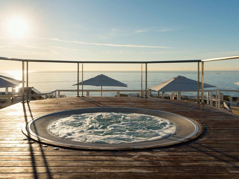 Outdoor jacuzzi on wooden deck with umbrellas and sunrise view over the sea.