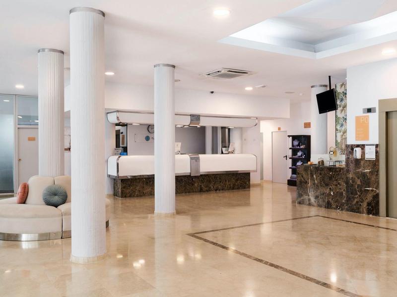 Spacious hotel lobby with polished floors, reception desk, columns, and seating area under bright lights.