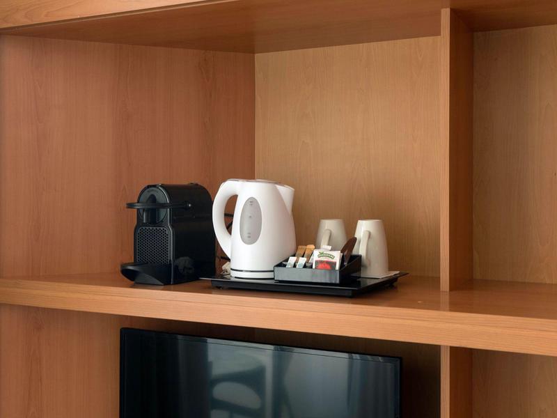 Coffee machine, electric kettle, cups, and tea setup on wooden shelf above TV.