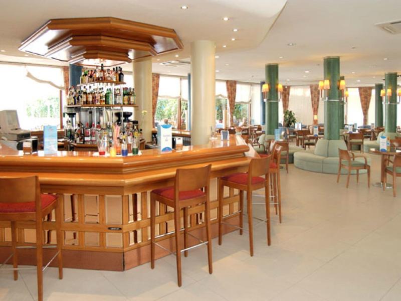 Spacious hotel bar with wooden counter, high stools, and tables with chairs in a bright area.