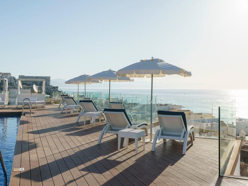 Sun loungers and umbrellas on a wooden deck by a pool overlooking the sea at sunrise.