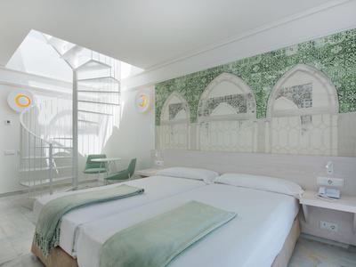 Modernes Hotelzimmer mit Doppelbett, grünem Wandbild und spiralförmiger Treppe zum Obergeschoss.