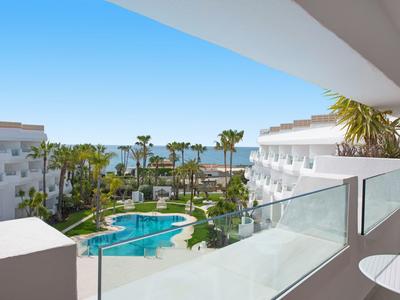 Blick von Hotelbalkon auf Pool, Garten mit Palmen und das Meer bei blauem Himmel.