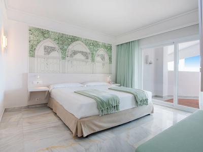 Helles Hotelzimmer mit Doppelbett, grünen Akzenten und Zugang zu einer sonnigen Terrasse.