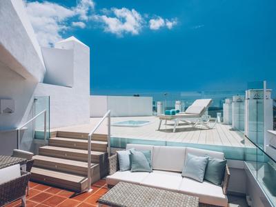 Moderne Dachterrasse mit Sitzecke und Pool, weiß-blauer Farbkontrast unter sonnigem Himmel.