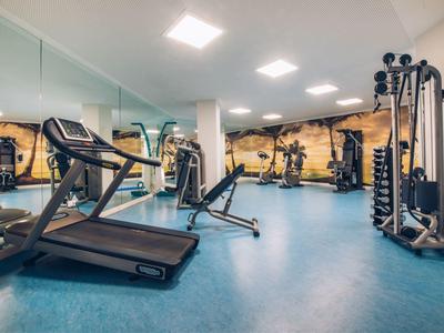 Moderner Fitnessraum mit Laufband, Rudergerät und Kraftstation, heller Raum mit Spiegelwand.