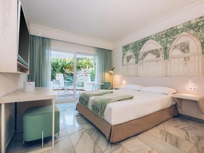 Helles Hotelzimmer mit Doppelbett, Schreibtisch, großem Wandbild und Zugang zu einer Terrasse.