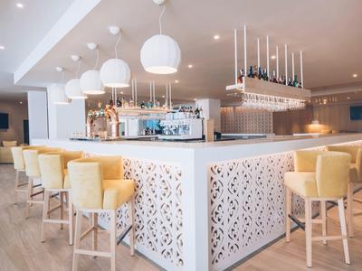 Helle Hotelbar mit weißen und gelben Stühlen, modernen Lampen und einem eleganten Tresen.