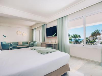 Helles Hotelzimmer mit großem Bett, Sitzecke und Meerblick durch Fenster.