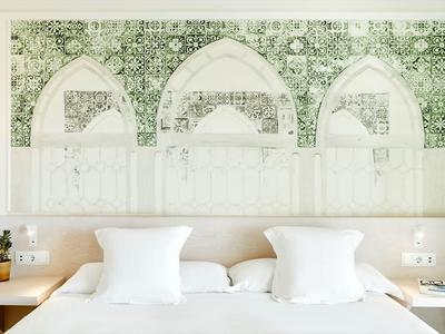 Hell eingerichtetes Hotelzimmer mit großem Bett, weißen Kissen und floralem Wandbild.