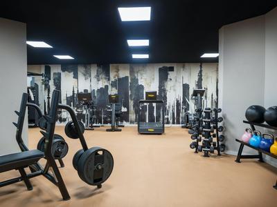 Moderner Fitnessraum mit verschiedenen Trainingsgeräten und Hanteln in einem Hotel.