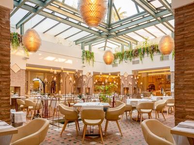 Helles Hotelrestaurant mit Glasdach, stilvollen Lampen und runden Tischen in warmen Farben.