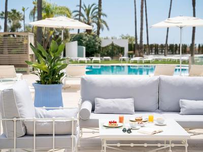Moderne weiße Lounge-Möbel mit Tisch und Pool im Hintergrund bei sonnigem Wetter.