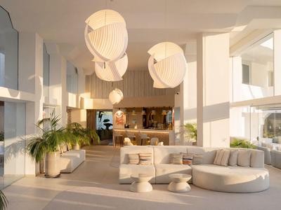 Hell eingerichtete Hotellobby mit großen Fenstern, modernen Möbeln und weißen Hängelampen.