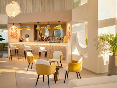 Heller, moderner Hotelbarbereich mit gelben Sesseln und Barhockern vor einer beleuchteten Theke.