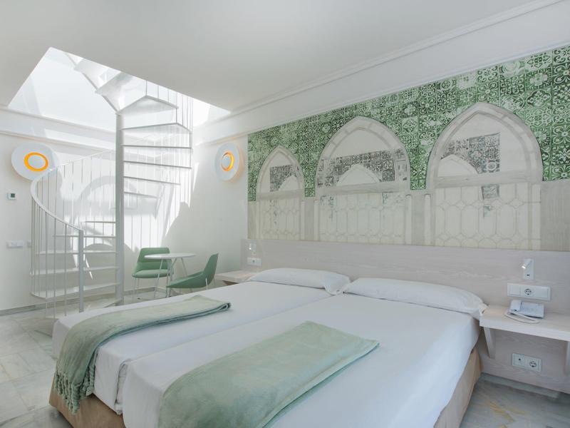 Bright hotel room with double bed, antique arcade mural, and modern staircase in the background.