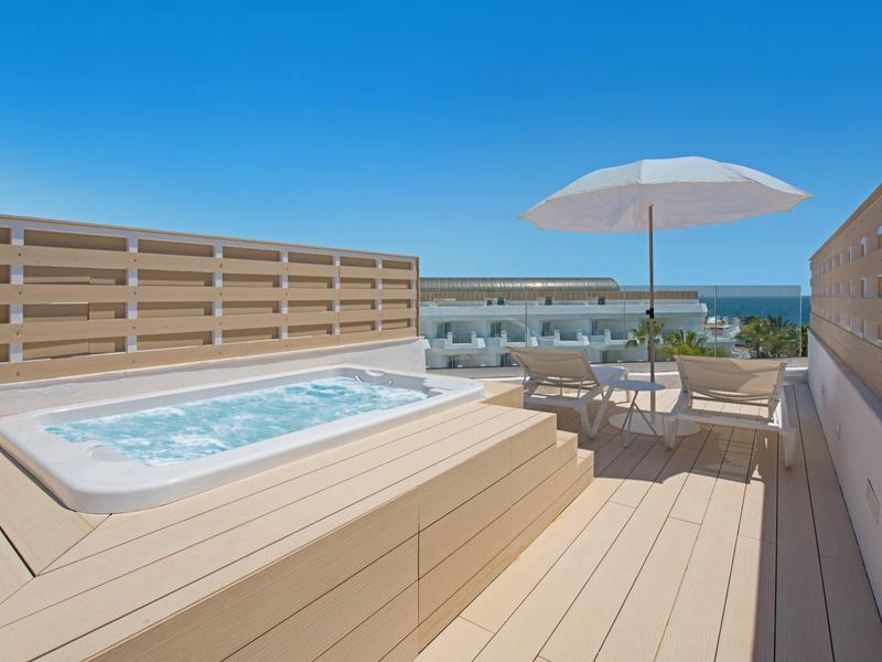 Rooftop terrace with a hot tub, sun umbrella, and seating area overlooking the sea.