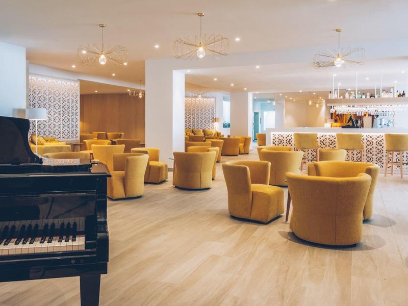Bright hotel lounge area with yellow armchairs and black piano.