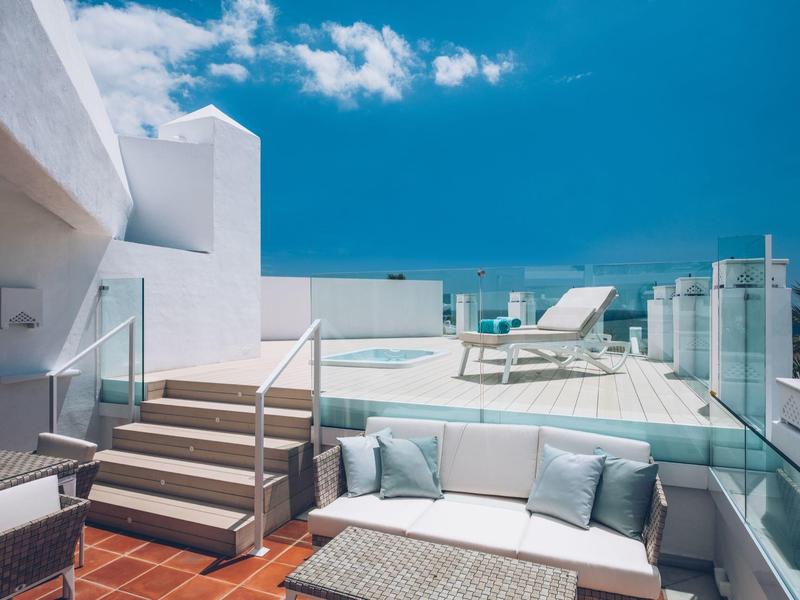 Modern rooftop terrace with white furniture and sun loungers under a blue sky.