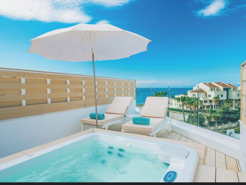 Small hot tub on a sunny terrace with lounge chairs and ocean view.