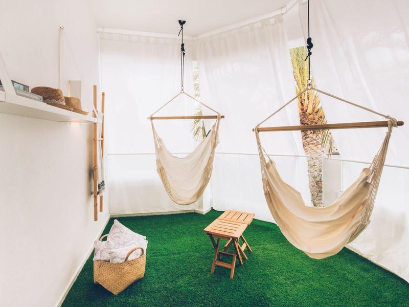 Brightly lit room with two hanging chairs, clothing rack, and grass-like carpet.
