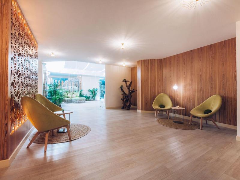 Bright hotel corridor with modern chairs, wood paneling, and a view of green plants.