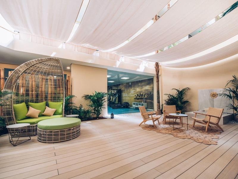 Cozy lounge area with chairs, sofa, and plants on wooden deck under bright fabric canopy.