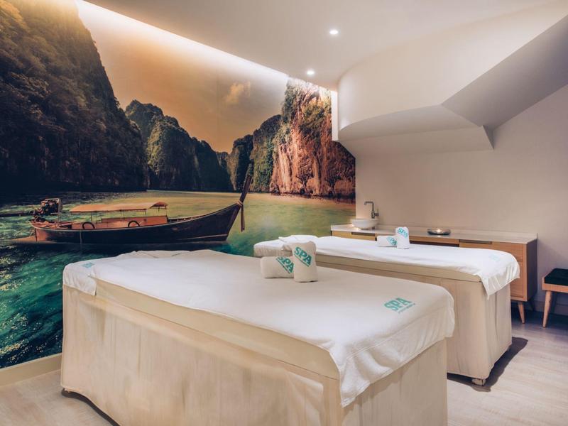 Modern wellness room with two massage beds and a tropical coastline wall mural.