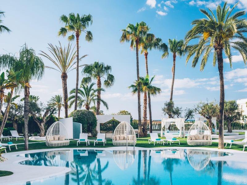 Beautiful pool area with palm trees and lounge chairs under a blue sky.