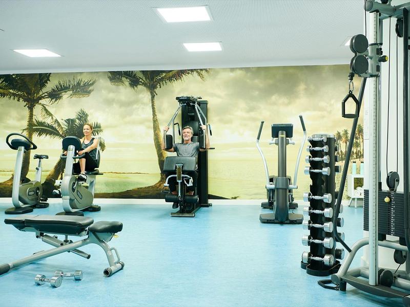 Bright gym with modern workout equipment and tropical wall mural.