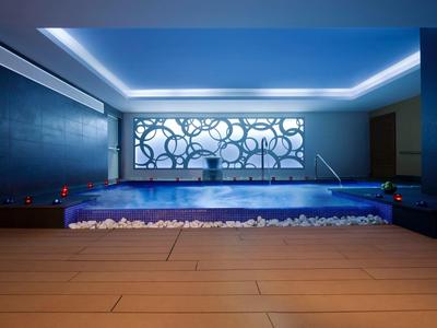 Modern indoor pool with illuminated water and decorative wall design in blue hues.