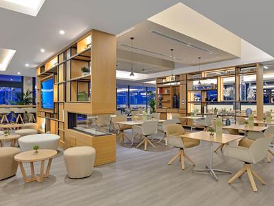 Bright modern hotel dining area with wooden and cream furniture and large windows.